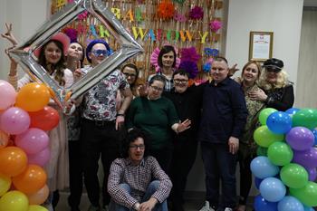 Uczestnicy oraz kadra w strojach karnawałowych na tle złotych serpentyn i kolorowych balonów